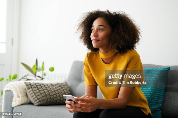woman looking up with smart phone on sofa - yellow sofa stock pictures, royalty-free photos & images
