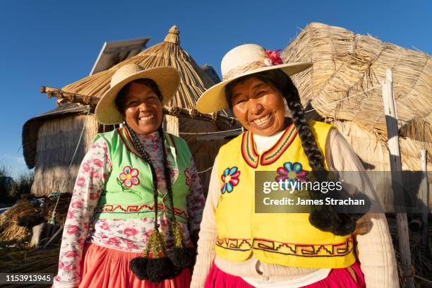 two uros women with braids and wearing colourful local traditional clothing on their floating island near puno, lake titicaca, peru (model releases) - puno stock pictures, royalty-free photos & images