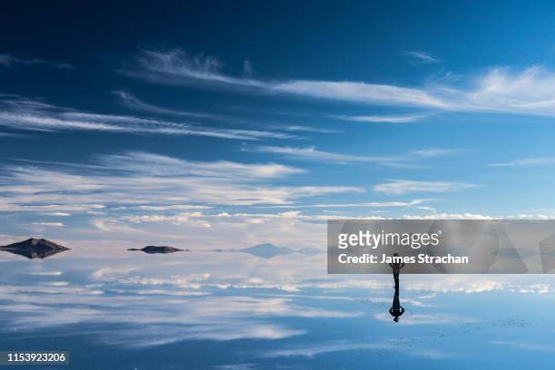 lone, silhouetted traveler in safari hat stops to admire the beauty of the salt flats which are reflecting the clouds and mountains after rainfall, uyuni, bolivia - saltäng bildbanksfoton och bilder