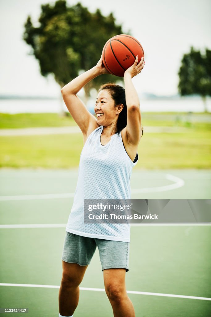 Smiling mature woman looking to make pass during basketball game on outdoor court