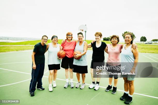 Portrait of smiling senior and mature women standing on outdoor basketball court after game