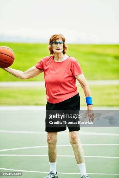 Portrait of senior woman dribbling basketball during early morning game on outdoor court