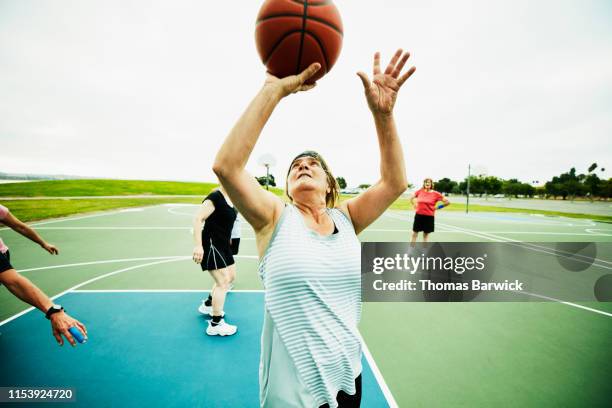 mature woman shooting layup during basketball game on outdoor court - pre game stockfoto's en -beelden