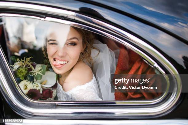 beautiful bride shows tongue sitting in the car - bruid stockfoto's en -beelden