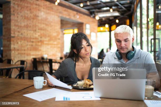 colleagues analyzing some data from digital investment on mobile phone and laptop - coffee shop couple stock pictures, royalty-free photos & images