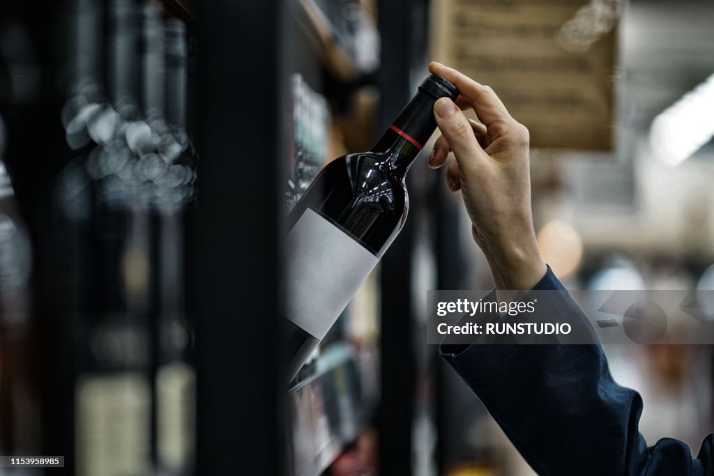 Woman choosing wine bottle in liquor store