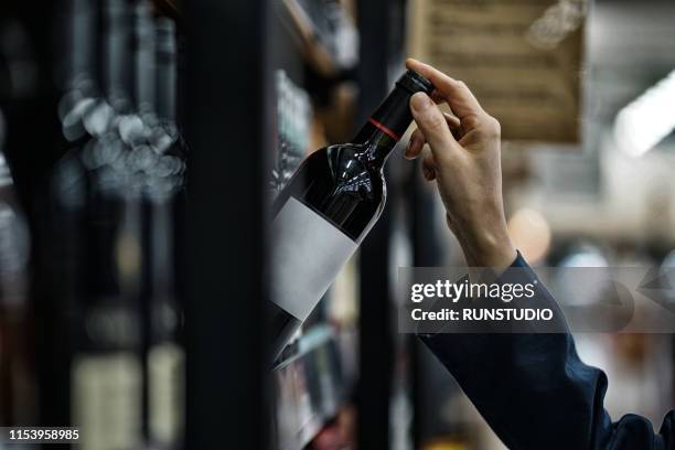 woman choosing wine bottle in liquor store - vinos fotografías e imágenes de stock