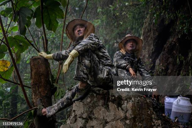 Helpers watch and wait as Chinese ethnic Lisu honey hunters, not seen, gather wild cliff honey from hives in a gorge on May 11, 2019 near Mangshi, in...