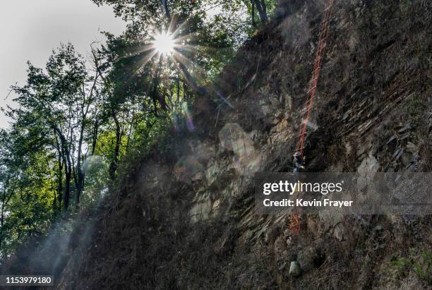 Chinese ethnic Lisu honey hunters Dong Haifa hangs on a makeshift ladder while gathering wild cliff honey from hives in a gorge on May 30, 2019 near...