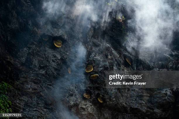 Smoke is seen around hives where Chinese ethnic Lisu honey hunters were gathering wild cliff honey in a gorge on May 10, 2019 near Mangshi, in Dehong...