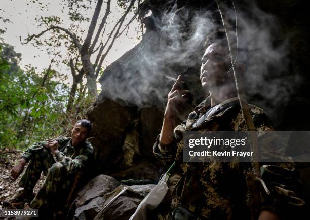 Chinese ethnic Lisu honey hunter Mi Qiaoyun, left, and helper Dongwu smoke as thye rest after gathering wild cliff honey from hives in a gorge on May...