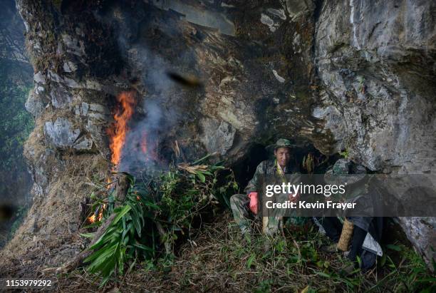 Chinese ethnic Lisu honey hunters Mi Qiaoyun, right, and Ma Yongde sit still next to a fire they set to deter bees before gathering wild cliff honey...