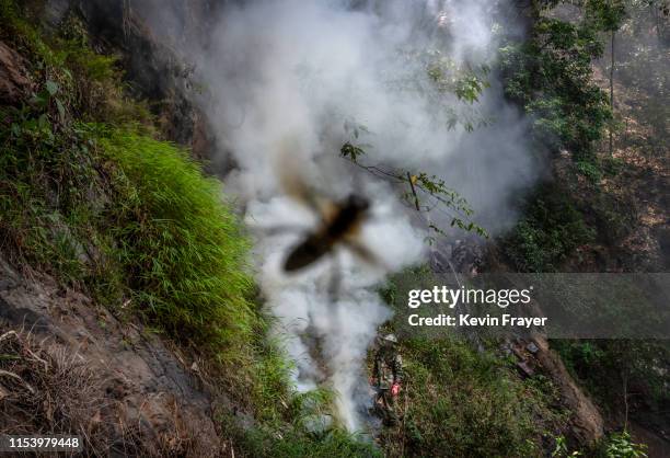 Chinese ethnic Lisu honey hunter Ma Yongde walks in smoke after making a fire before gathering wild cliff honey from hives in a gorge on May 11, 2019...