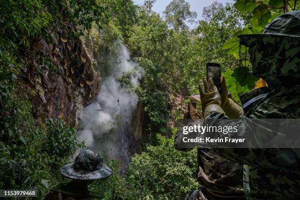 Helpers and a honey buyer take photos as Chinese ethnic Lisu honey hunters, not seen, gather wild cliff honey from hives in a gorge on May 11, 2019...