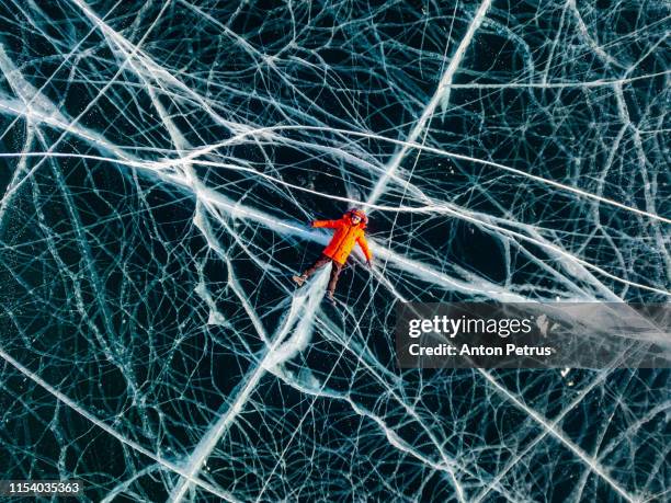 the guy in the red jacket is lying on the transparent ice. baikal, aerial view - baikal stock-fotos und bilder