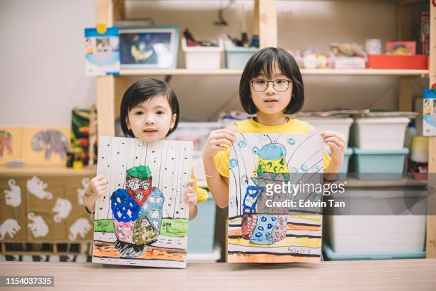 2 asian chinese children displaying their painting after the class at the art center looking at the camera - art product stock pictures, royalty-free photos & images