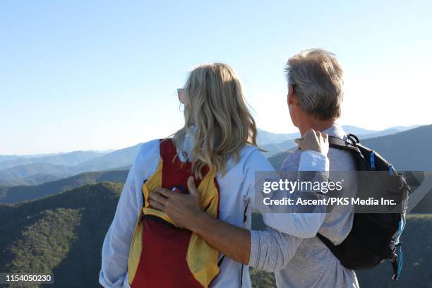 mature couple of hikers embrace on the top of a lush hill top and look out - gray hair couple stock pictures, royalty-free photos & images