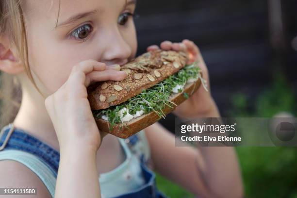 girl biting into a healthy brown bread roll stuffed with cream cheese and cress - lunch cheese stock-fotos und bilder