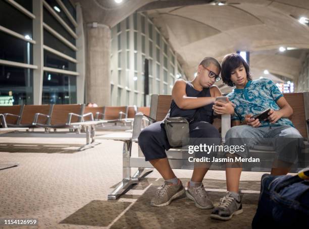 two boys sitting in an airport terminal - airport sitting family stock pictures, royalty-free photos & images