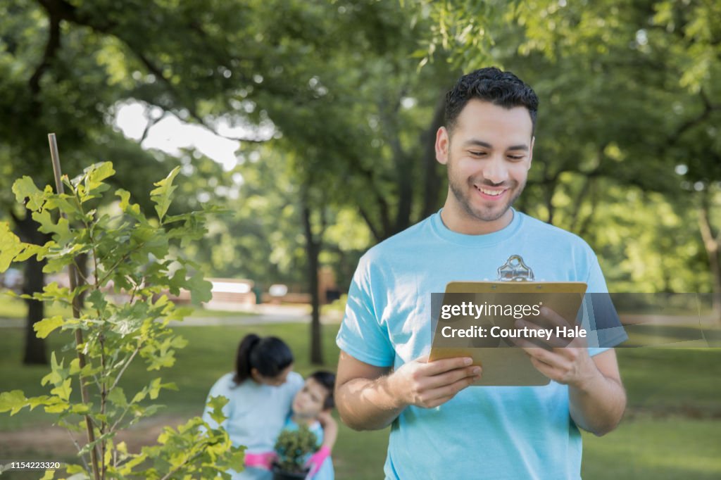 Young Hispanic man is leading group of volunteers to plant trees in public park