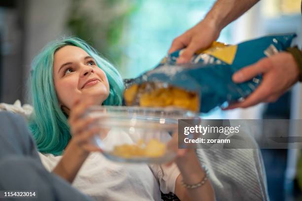 anime-like young woman on the sofa holding bowl for more potato chips - chips bag stock pictures, royalty-free photos & images