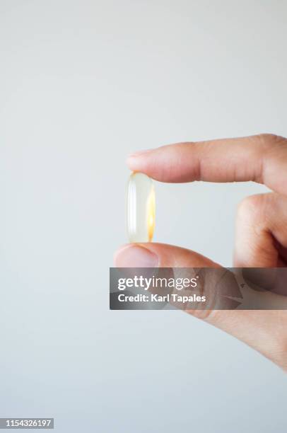 a young person's hand holding a medicine gel capsule on a white background - fish oil stock pictures, royalty-free photos & images