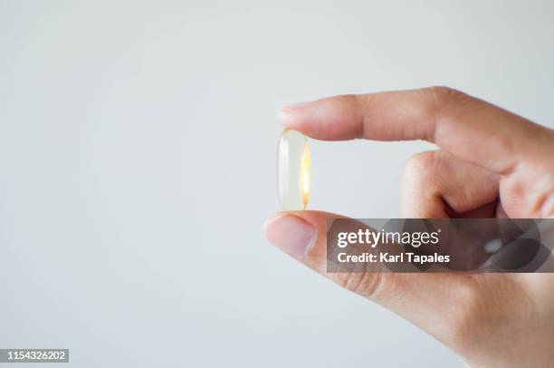 a young person's hand holding a medicine gel capsule on a white background - translucent stock pictures, royalty-free photos & images