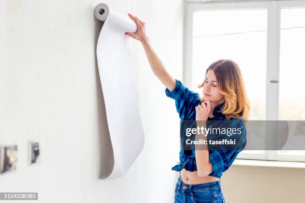 jonge vrouw kiezen huis behang - vrouw behangen stockfoto's en -beelden