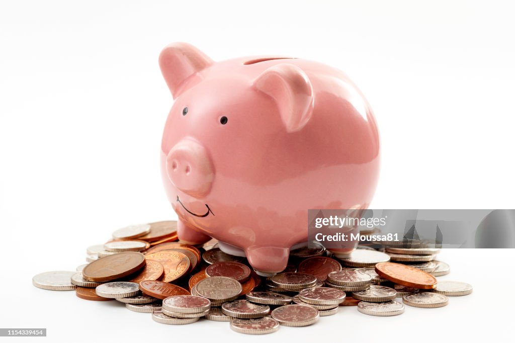 省錢, 個人財務的財務規劃和節儉的概念主題與粉紅色的存錢罐坐在一堆青銅和銀色硬幣孤立在白色的背景