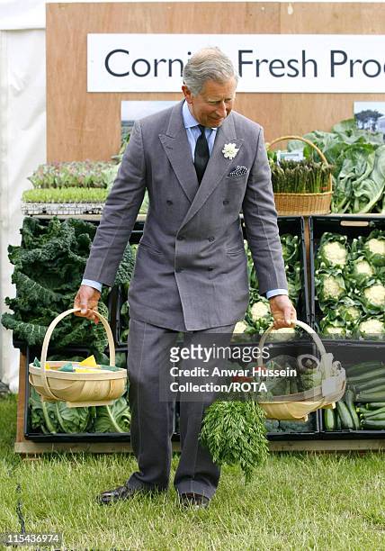 Prince Charles, the Prince of Wales, pretends to struggle under the weight of two baskets of fresh vegetables given to him during a visit to...