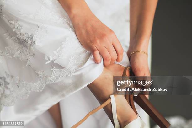the bride, girl or young woman in a beautiful elegant modern stylish wedding dress puts on a leg light leather fashionable high-heeled shoes, close-up. the day of the wedding or the morning. - girls high heels stock-fotos und bilder