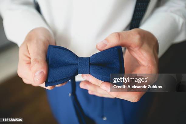 a man, a groom or a businessman in a stylish suit holding a blue bow tie, a fashion accessory. preparing the groom for the wedding day. blurred background, close-up. - 蝶ネクタイ ストックフォトと画像