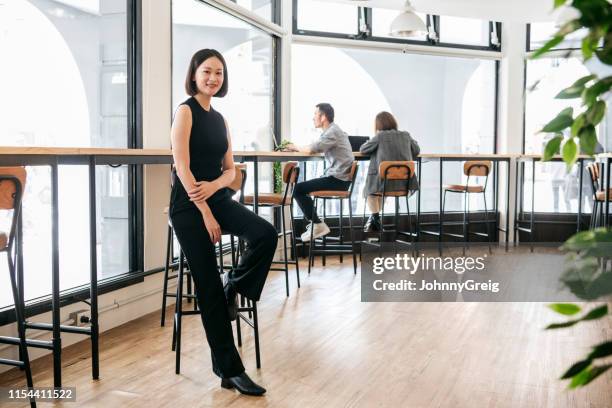 elegante frau sitzt auf hocker im offenen büro - happy asian woman bright office stock-fotos und bilder