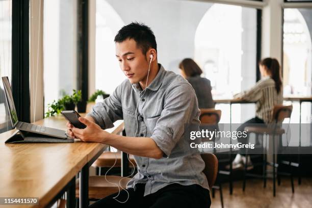 trabajador freelance usando auriculares y mensajes de texto en el teléfono inteligente - headphones asian fotografías e imágenes de stock