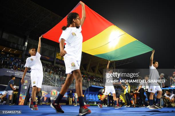 Egyptian children hold Guinea's national flag prior to the 2019 Africa Cup of Nations Round of 16 football match between Algeria and Guinea at the 30...