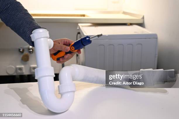 man holding a screwdriver in his hand, fixing the connecting tube of the kitchen water.  plumbing work at home - hose stockfoto's en -beelden