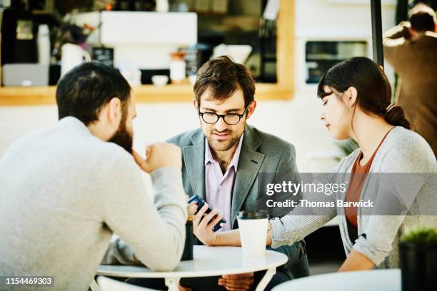 businesswoman showing colleagues information on smart phone during meeting at outdoor coffee shop - data trust stock pictures, royalty-free photos & images