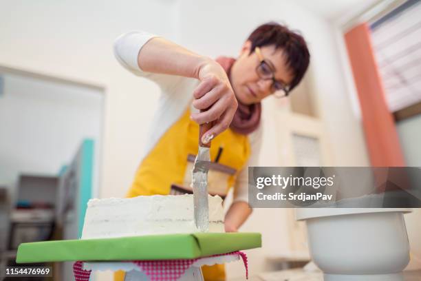 mujer poniendo glaseado con espátula - decorating a cake fotografías e imágenes de stock