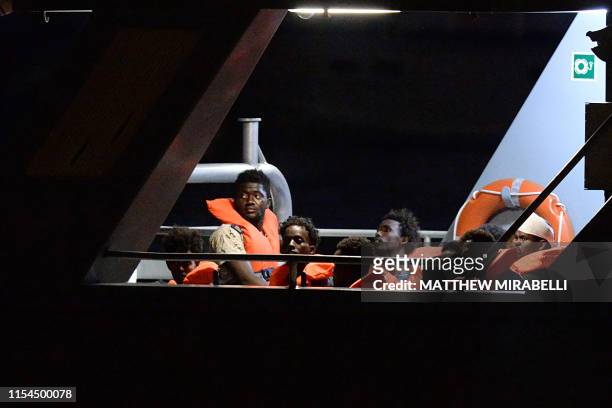 Migrants, part of group of 65 rescued by the German-flagged NGO rescue ship Alan Kurdi, look out from a patrol boat as they are brought into...