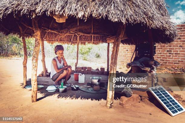 una mujer joven que cocina laberinto de maíz bajo una choza en un pueblo africano - africa fotografías e imágenes de stock