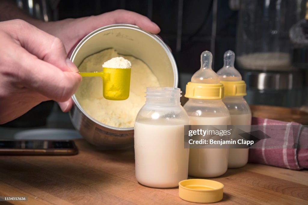 Hand holding scoop of powdered baby formula, ready to mix in bottles