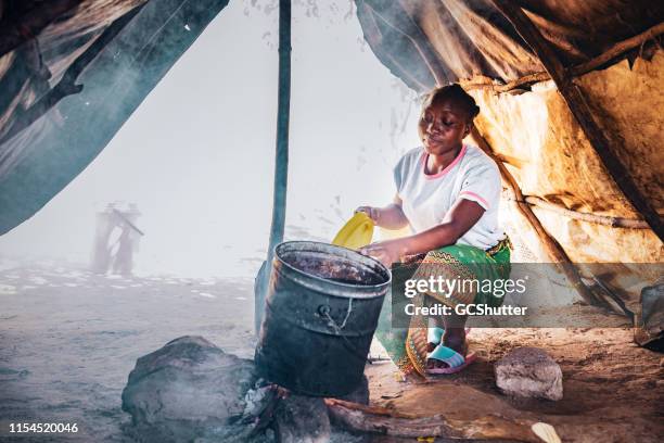 une femme africaine bouillante l’eau sur le feu de bois - daily bucket photos et images de collection