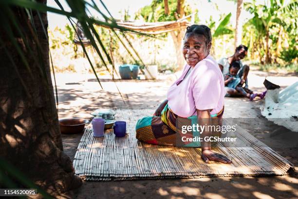 een afrikaanse vrouw zittend op een rietje mat, keert terug naar de camera voor een portret - zambia stockfoto's en -beelden