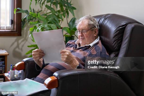 senior man sitting in his recliner whilst reading the newspaper in his lounge room. - recliner chair stock pictures, royalty-free photos & images