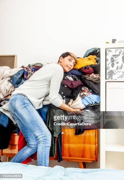 woman holding a heap of clothes preventing to fall down - overflowing closet stock pictures, royalty-free photos & images