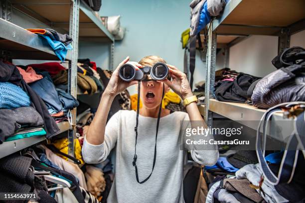 conceptual image of a woman using binoculars to find clothing in the messy closet - overflowing closet stock pictures, royalty-free photos & images
