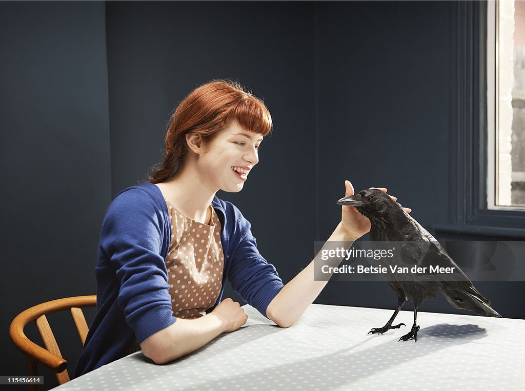 Woman stroking crow standing on table.