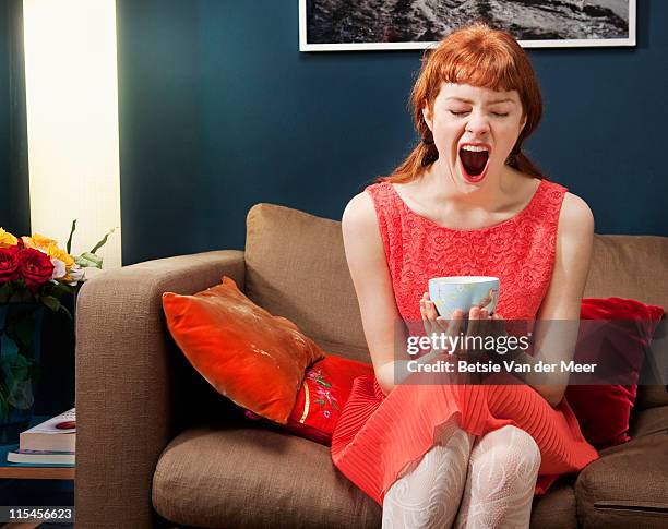 woman sitting on sofa, yawning. - yawning stock-fotos und bilder