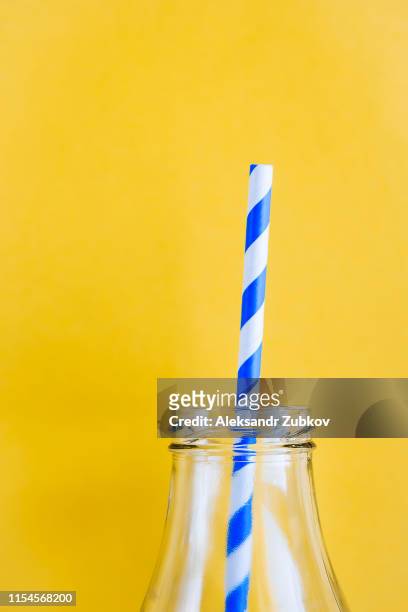 Colored, reusable, paper, striped, blue and white straws for drinking juice or cocktail life, in a glass bottle, on a yellow background. The concept of the festival, healthy eating, no plastic.