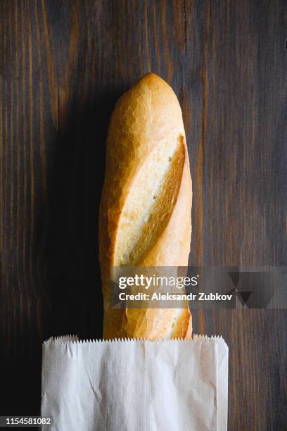 freshly baked bread in a paper bag or package, on a cutting board, on a brown wooden table, close-up. copy space for text. the concept of organic farming food, no plastic. - baguette photos et images de collection